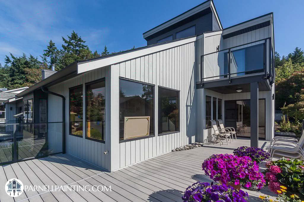 A west coast style house with cedar siding is painted with a light gray and dark chacoal accents to compliment the black windows.